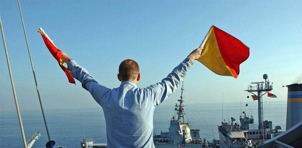 A US Navy crewman signals the letter 'U' using flag semaphore during an underway replenishment exercise (2005)